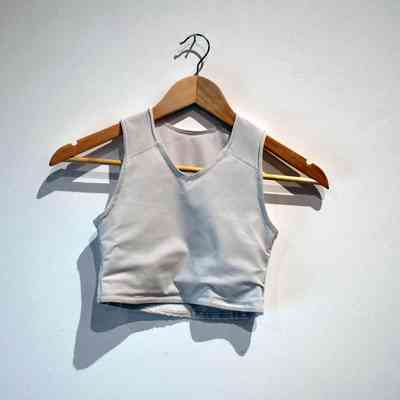A light gray crop top on a wooden hanger is displayed against a plain wall.