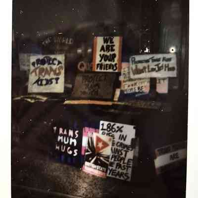 Lots of protest signs propped up together against a fence at night time.