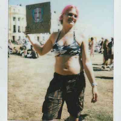 A person with pink hair holds a hand-drawn sign which says "UP THE TRA".