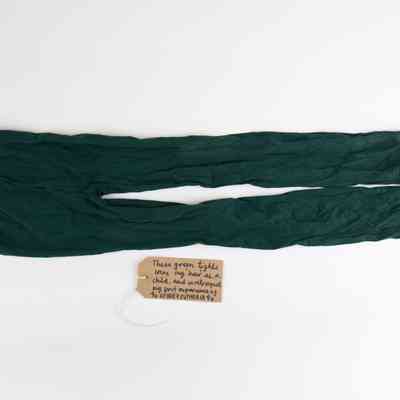 A pair of dark green opaque tights. With a brown, handwritten luggage tag.