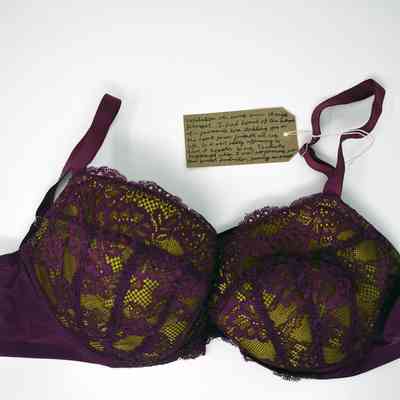 A burgundy lace bra lies on a white background, accompanied by a small handwritten note.