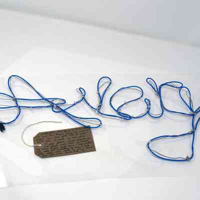 Blue wire spelling "Rock" lies on a surface, accompanied by a handwritten tag.