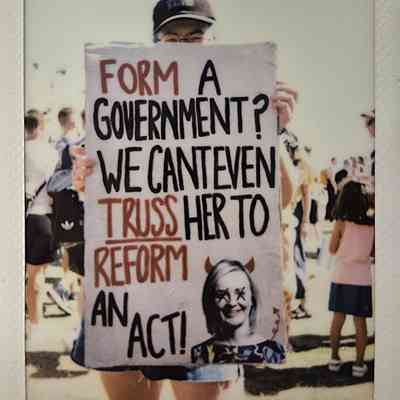A person holds a protest sign with bold text which says "FORM A GOVERNMENT? WE CAN'T EVEN TRUSS HER TO REFORM AN ACT!".
