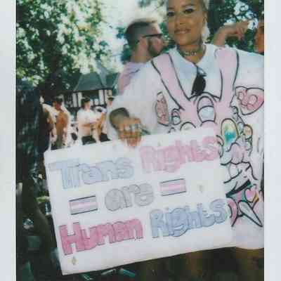A person is holding a colorful sign that states "Trans Rights are Human Rights" at an outdoor event