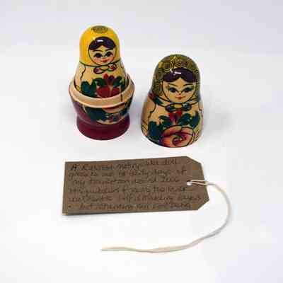 A russian doll which has the first head taken off so you can see the inside doll. It is colourfully painted in reds, yellows and greens.