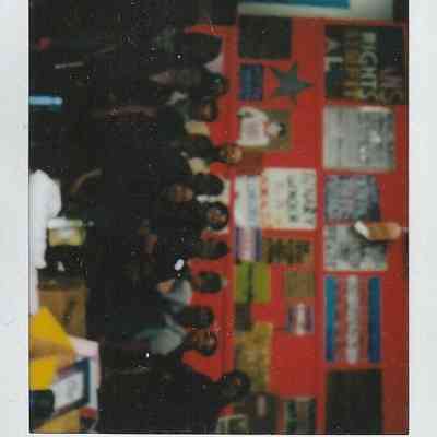 A group of people gathers in front of a colorful wall filled with various posters and signs.