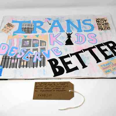 An A3 sketch pad with a hand painted Trans Kids Deserve Better poster. It features smaller paintings of other placards and scenes from the Department for Education Occupation/Encampment and a blue tardis. With a brown, handwritten luggage tag.