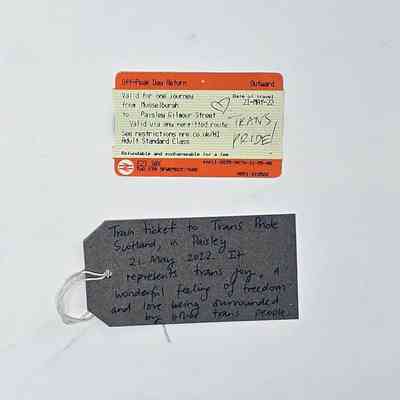 A train ticket which has 'Trans Pride' written in biro on it with a hear. Underneath there is a brown tag with writing on it.