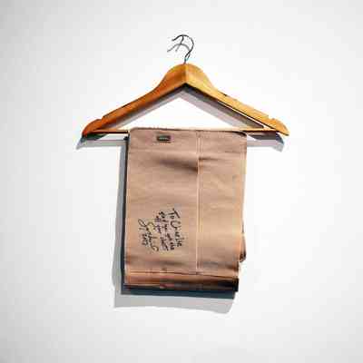 A wooden hanger displays folded beige fabric with handwritten notes on a plain white wall.