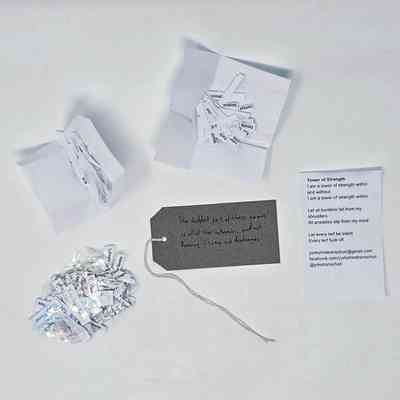 Plastic sleeve containing a bundle of small strips of paper, a poem titled "Tower of Strength", several white strips of paper, and a brown tag.