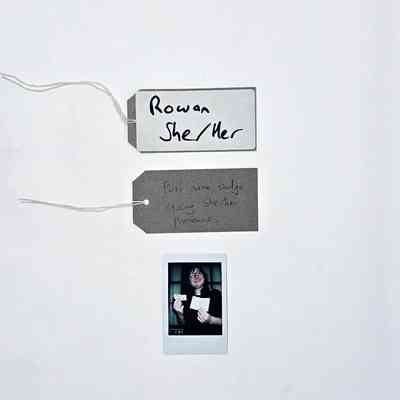 A handwritten name tag inscribed "Rowan" "She/Her". With a brown handwritten luggage tag.