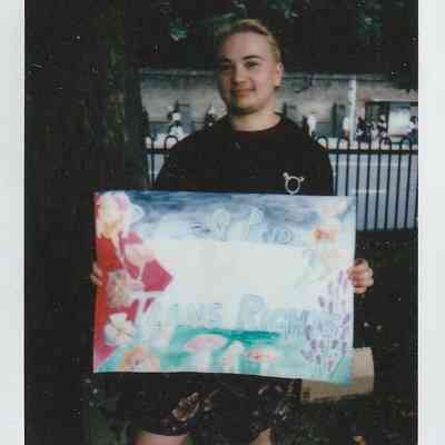 A person holds a colorful sign that reads, “Peace and Pride, Trans Rights".