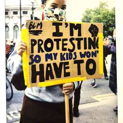 A protester wearing a mask holds a sign that says, "I'm protesting so my kids won't have to".
