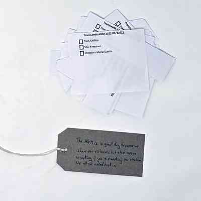 Stack of white voting slips over a brown tag reading "The AGM is a great day because we share our victories, but also nerve wracking if you're standing for election!
We all got voted back in"