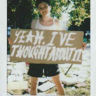 A person stands outdoors holding a sign saying, "YEAH, I'VE THOUGHT ABOUT IT".