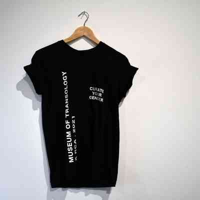 A black T-shirt on a hanger features the text "CURATE YOUR GENDER" and "Museum of Transology".