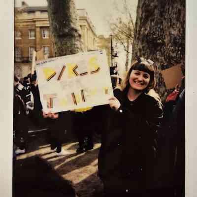 A person is joyfully holding a sign that says "Dykes for Trans" during an outdoor gathering.