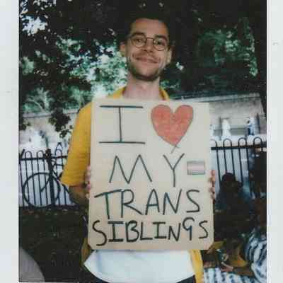 A person is smiling while holding a sign that says, "I love my trans siblings".