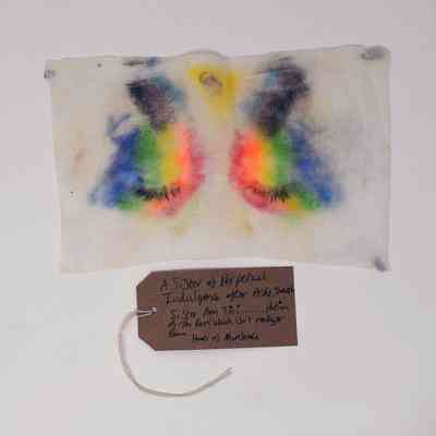 A used makeup wipe showing the remnants of colourful makeup. With a brown, handwritten luggage tag.