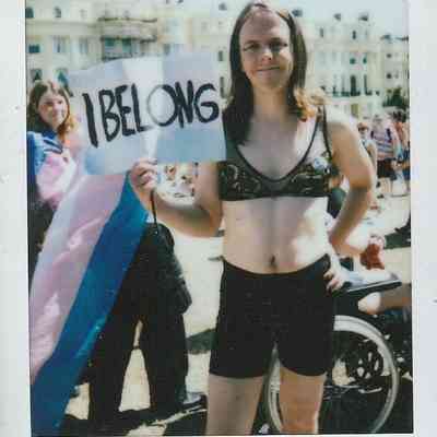 A person stands confidently holding a sign saying "I belong" at an outdoor event.