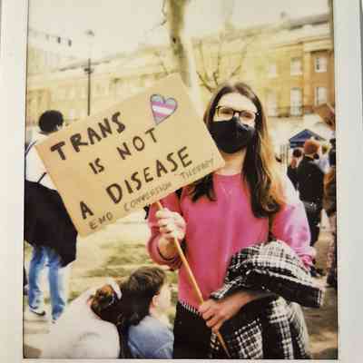 A person holding a sign which says "TRANS IS NOT A DISEASE END CONVERSION THERAPY".