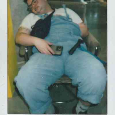 A person in overalls is asleep in a chair, holding a phone, looking quite comfortable and relaxed.