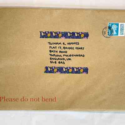 An opened brown envelope decorated with purple tape with flowers and fruit on. It has a franked 1st class stamp and the next "Please do not bend". It is addressed to the donor, Twinam R Hughes.