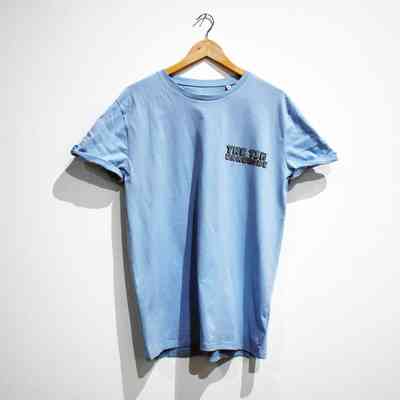 A light blue t-shirt with "THE TIN WARDROBE" printed on the breast on a wooden hanger.