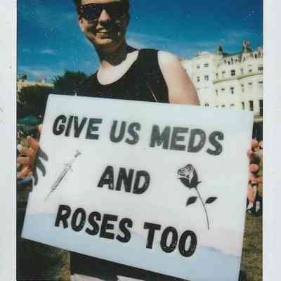 A person holding a sign reading, "Give us meds and roses too".