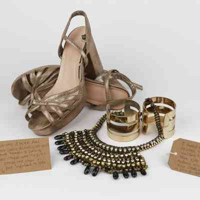 The image shows gold high heels, a statement necklace, and wide bracelets, accompanied by handwritten tags.