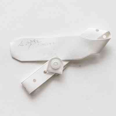 A white plastic garment tag with a circular, hole-punched fastener is placed against a plain background