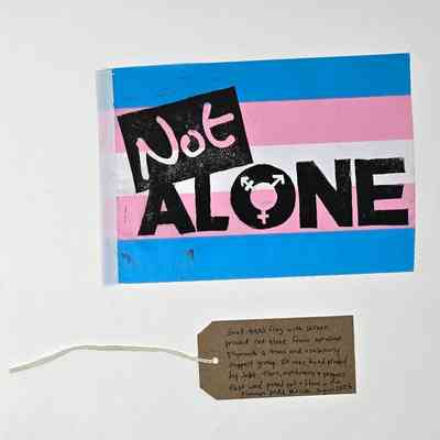 A poster with "Not Alone" text on a transgender flag background, featuring a note attached.
