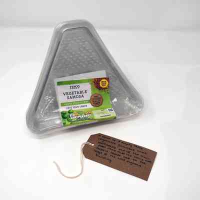 The image shows an empty triangle samosa package with a handwritten note beside it.