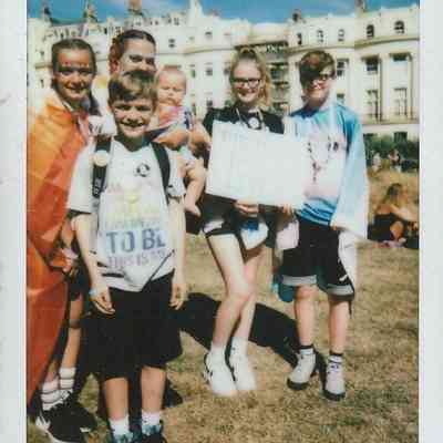 A group of people stand together, smiling outdoors, some holding protest signs.