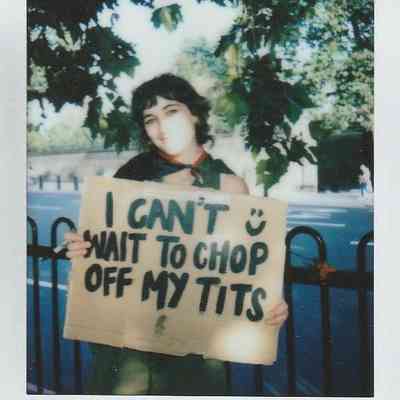 A person stands outdoors holding a sign expressing a personal message in front of trees.