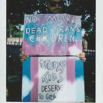A person holds two signs with supportive messages for trans youth at Trans Pride event.