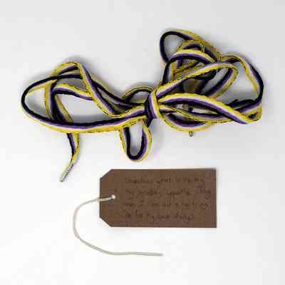 A bundle of colorful shoelaces lies next to a handwritten tag on plain background.