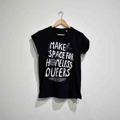A black T-shirt with the text 'Make Space For Homeless Queers' hangs on a wooden hanger.