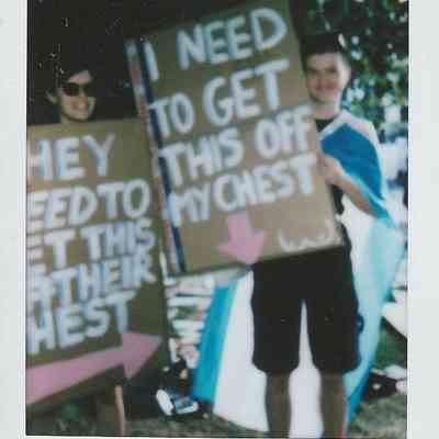Two people are holding signs with bold messages while standing outdoors wearing different colored clothing.
