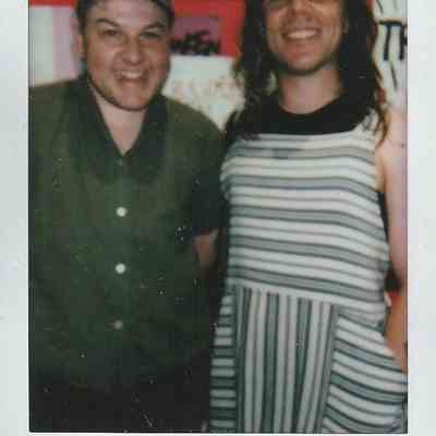 Two people are smiling in front of colorful signs, with "Transcestry, '28".