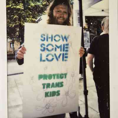A person holds a sign reading "Show Some Love, Protect Trans Kids" during a pride.