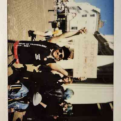 A person happily holds a sign reading “donate your signs here” while standing on a street.