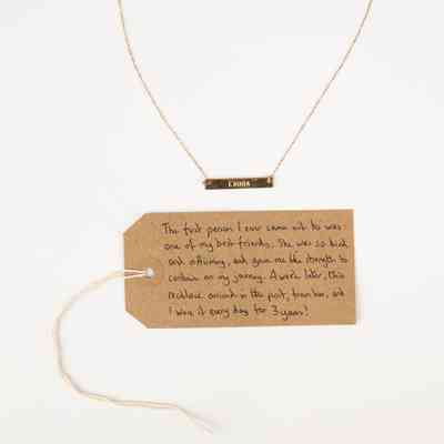 A gold necklace with name "LAURA". With a brown, handwritten luggage tag.