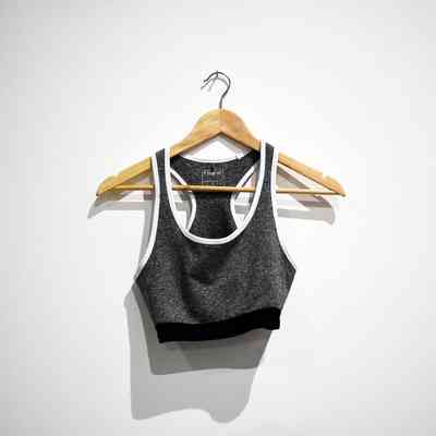 A gray sports bra with white trim hangs on a wooden hanger against a plain wall.