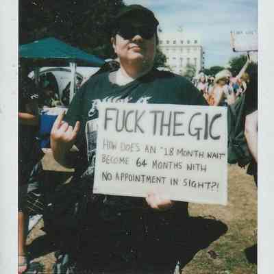 A person is holding a protest sign which says "Fuck The GIC".