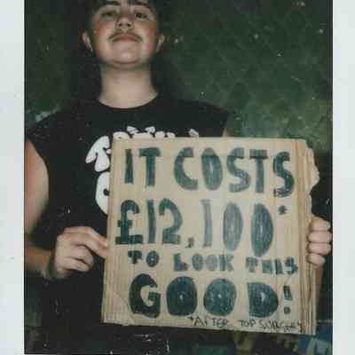 A person holds a cardboard sign that says "It costs £12,100 to look this good".