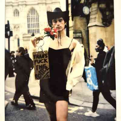 A person wearing a cowboy hat holds a sign and flowers during a street protest.