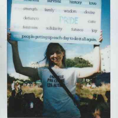 A person holds a sign with words like "realness" and "Pride," standing among a crowd of people.