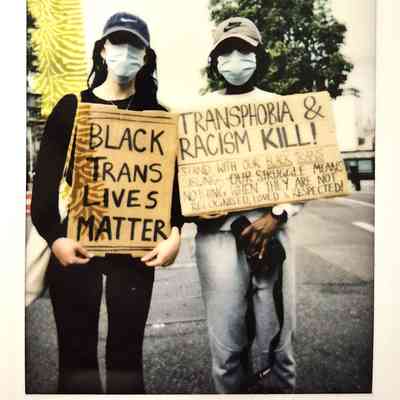 Two individuals at a protest hold signs advocating for Black trans lives and against transphobia and racism.