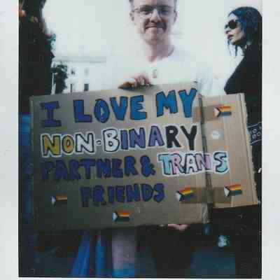 A person holds a placard which says "I Love My Non-Binary Partner & Trans Friends".